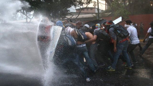 Protesters hold a barricade against a water cannon fired by the Venezuelan national guard during an anti-government demonstration