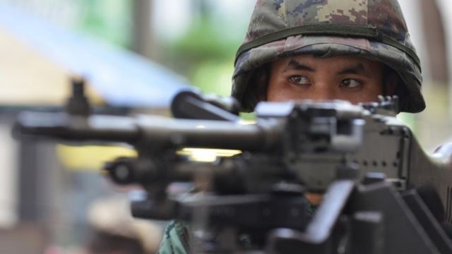 Thai army soldier stands guard on a city centre street.