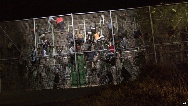 Sub-Saharan migrants scale a metallic fence that divides Morocco and the Spanish enclave of Melilla