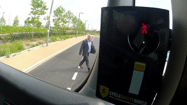 A man walks in front of a bus as part of a controlled demonstration of the Cycle Safety Shield device