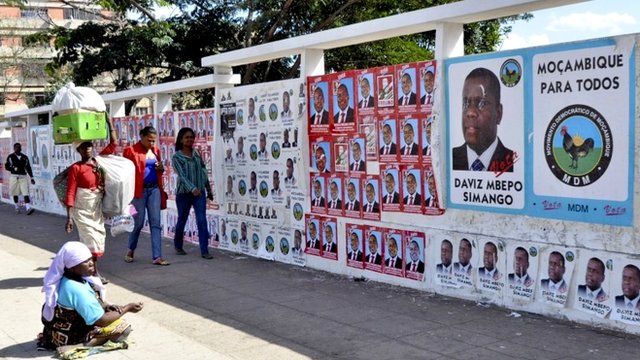 People walk pass a wall adorned with various election campaign posters