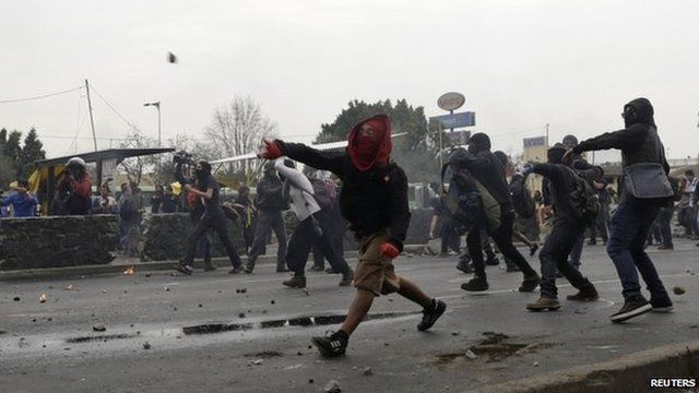 Masked demonstrators throw rocks towards riot police during a protest over the 43 missing Ayotzinapa students, near the Benito Juarez International airport in Mexico City on 20 November 2014.