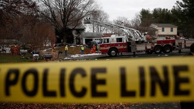 Utility workers and emergency personnel work near the site where a small plane crashed into a residential neighbourhood