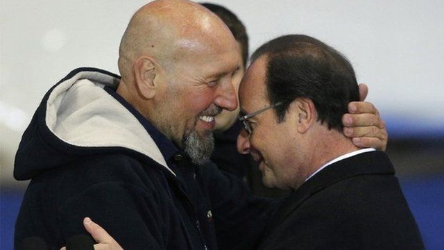 Serge Lazarevic (L) hugs French President Francois Hollande after he arrives at Villacoublay military airport (10 Dec)
