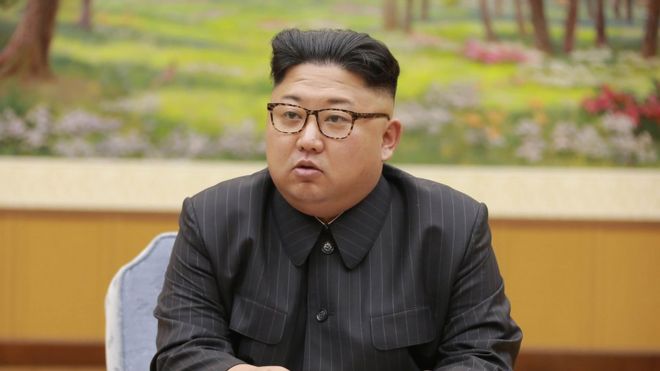 Kim Jong-un seen seated, wearing brown tortoiseshell glasses and a pinstripe dark grey suit