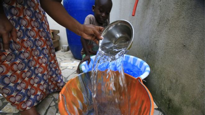 A woman fills a bucket with tap water in Abidjan, Ivory Coast as a small boy watches on.