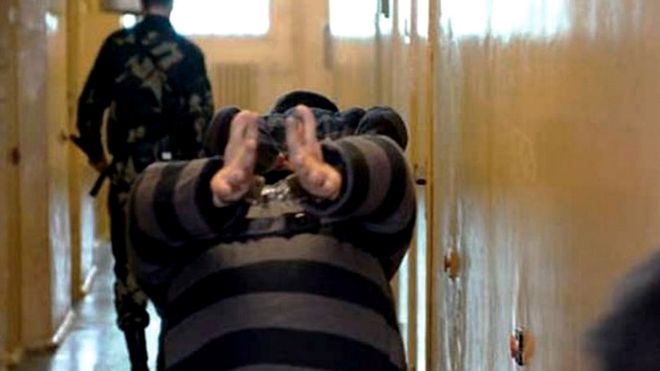 Un prisionero camina doblado viendo hacia abajo y con las manos esposadas en una prisión bielorrusa en 2006.