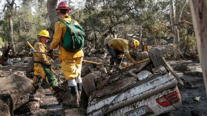 Rescue workers looking at an upturned car, surrounded by mud