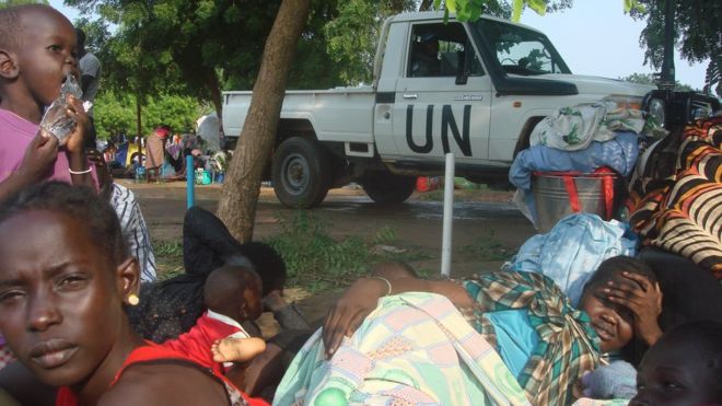 women and children sitting on the ground in front of a UN truck