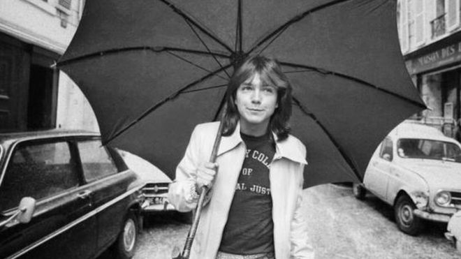 David Cassidy walking down a road in London with an umbrella (30 April 1974)