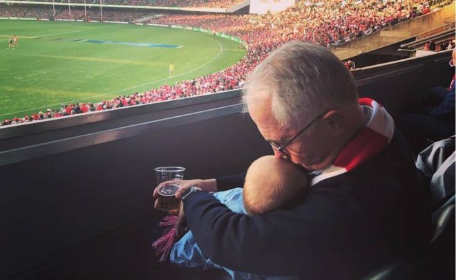 Malcolm Turnbull kisses his young granddaughter while holding her in one hand and a beer in another, at a sporting match in Sydney on Saturday