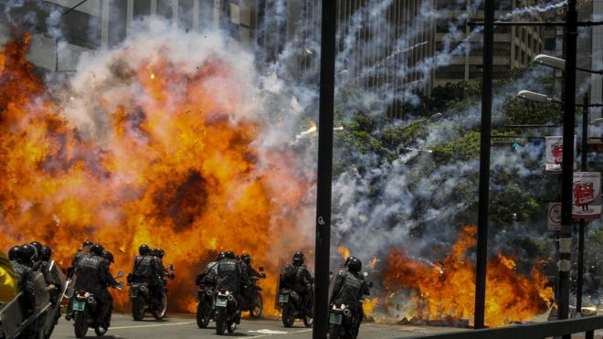 Una explosión en la zona de Altamira, en Caracas, mientras varios policías pasan por allí en motocicletas.