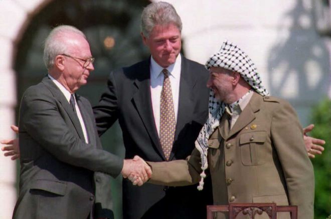 Prezydent USA Bill Clinton (w środku) stoi między liderem OWP Jaserem Arafatem (z prawej) izraelskim premierem Icchakiem Rabinem, jako dwoma uścisliwymi dłońmi.