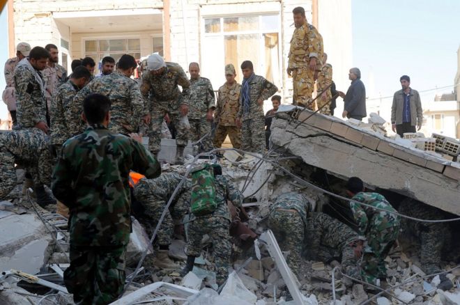 More than 20 soldiers around and under a slab of concrete in a pile of rubble