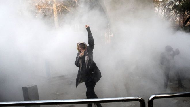 Иранская женщина поднимает свой кулак среди слезоточивого газа в Тегеранском университете во время протеста в столице 30 декабря 2017 года