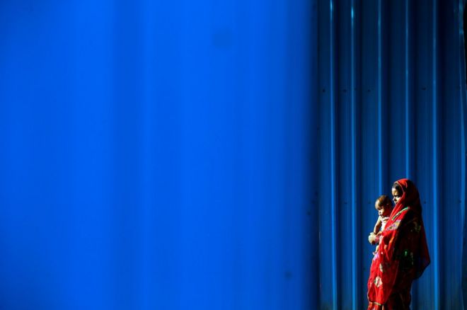 இந்தியாவின் தலைநகரான டெல்லியில் கட்டுமான இடத்தின் பக்கத்தில் தன்னுடைய குழந்தையோடு நிற்கும் தினக்கூலி பெண்ணொருவர்