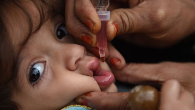 An adult hand uses a small syringe to drop oral Polio into a child's mouth in Karachi, Pakistan