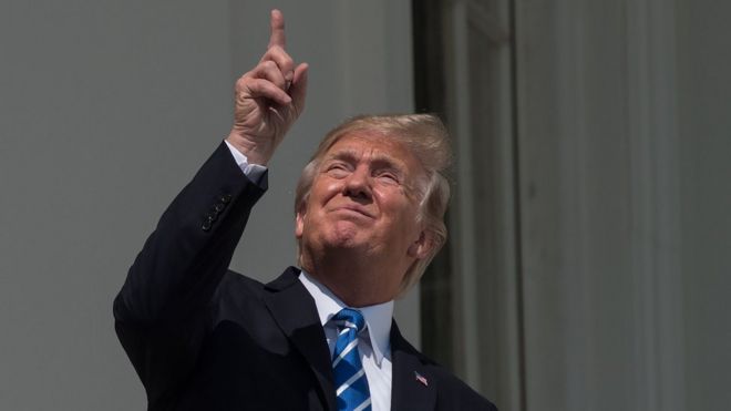 Trump señalando al cielo y mirando sin lentes el eclipse.
