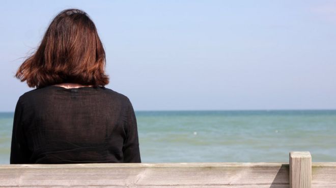 Mulher sozinha em banco na praia