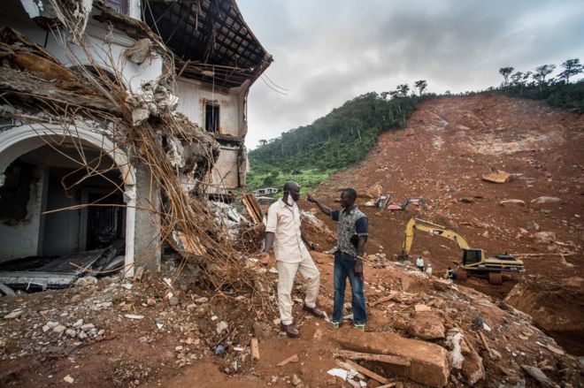 Alfred Johnny talks to friend beside the broken house and mudslide