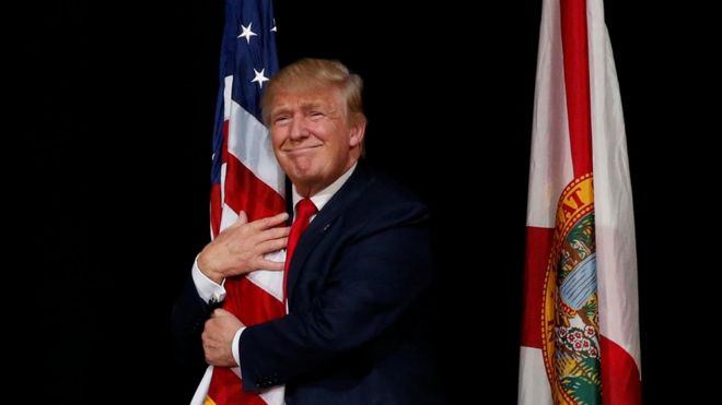 US presidential candidate Donald Trump hugs a US flag