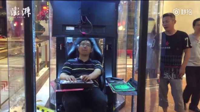 Man sitting in a pod, playing a computer arcade game at a shopping mall in China