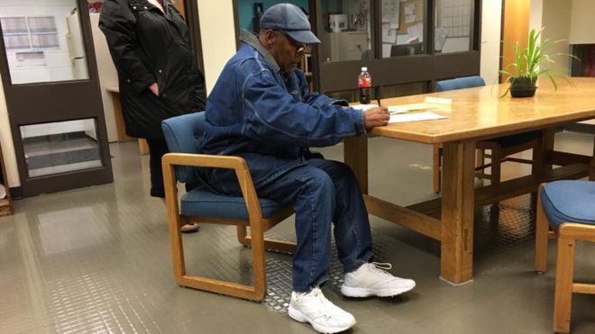 image of OJ being released from Nevada prison, wearing all denim signing a document on a table