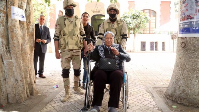 جنود يدفعون كرسي متحرك تجلس عليه امرأة مسنة