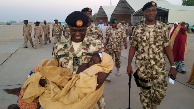 One of the released Dapchi school girls is carried as military and government officials supervise the airlift of the rescued girls at Maiduguri Airport, Nigeria