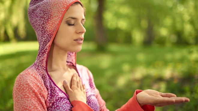 Joven meditando con una mano en su corazón y otra mano abierta y extendida