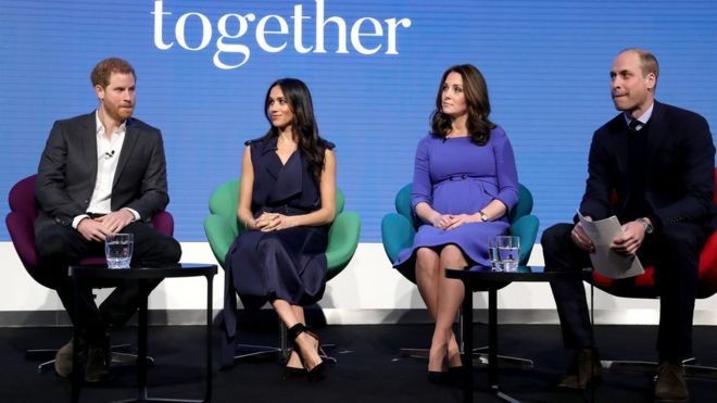 Harry, Meghan Markle, Kate Middleton e William sentados cada um em uma cadeira, em um palco