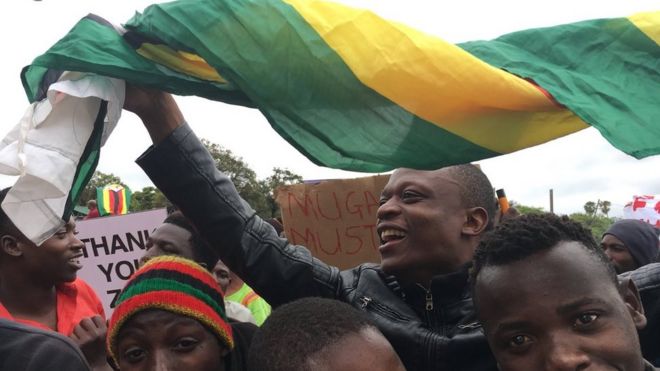 crowd with flag, sign reading Mugabe must go, people smiling