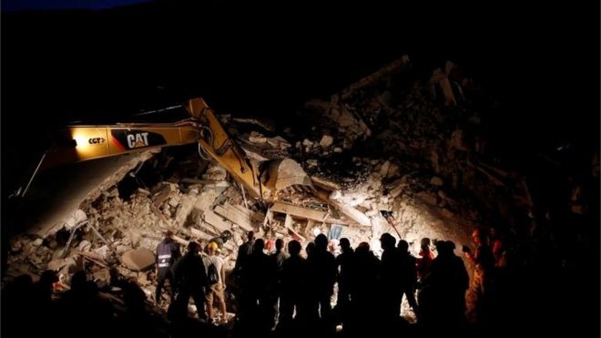 Rescatistas y máquinas excavadoras iluminadas en la noche.