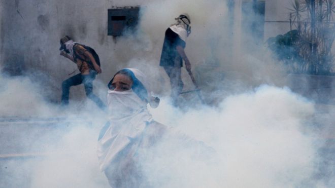 Manifestantes envueltos en una nube blanca de gas lacrimógeno en Caracas, Venezuela