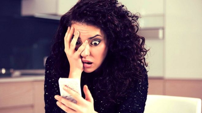 Mujer mirando un telÃ©fono celular con actitud angustiada.