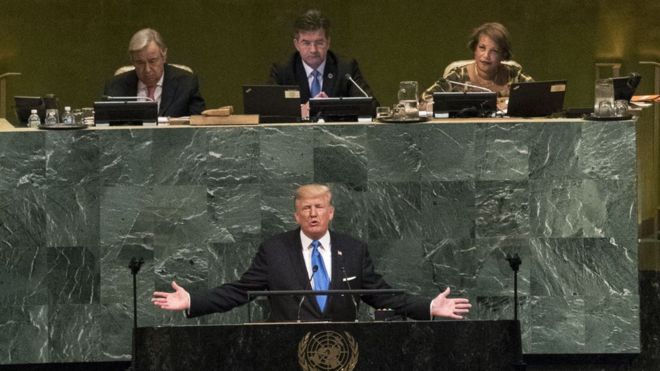 Donald Trump addresses the United Nations with outstretched arms in front of a podium emblazoned with the UN emblem