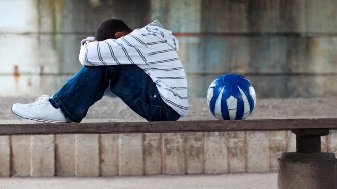 A boy sat with a ball, head in his hands