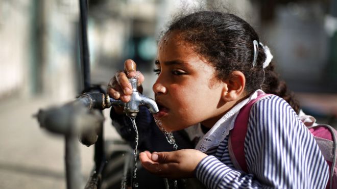 Niña tomando agua de una canilla en Gaza