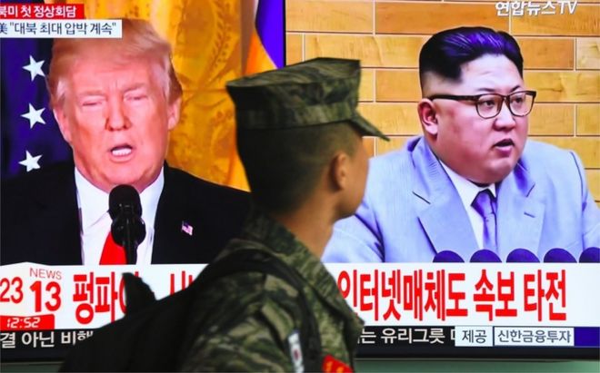 Un soldado surcoreano camina frente a una pantalla que muestra imágenes de Donald Trump y Kim Jong-un.