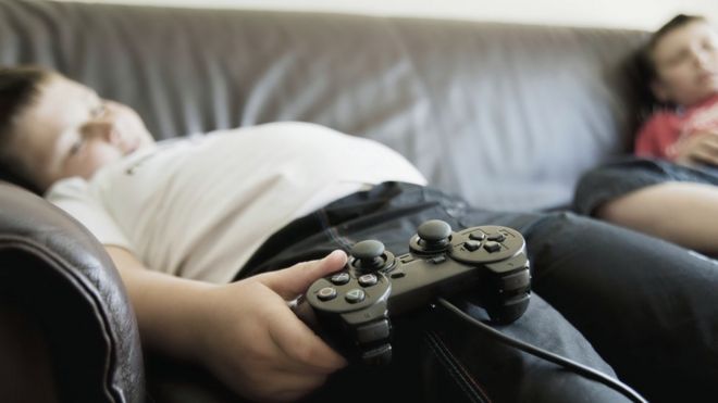 Garoto obeso sorme no sofá com o controle de videogame na mão
