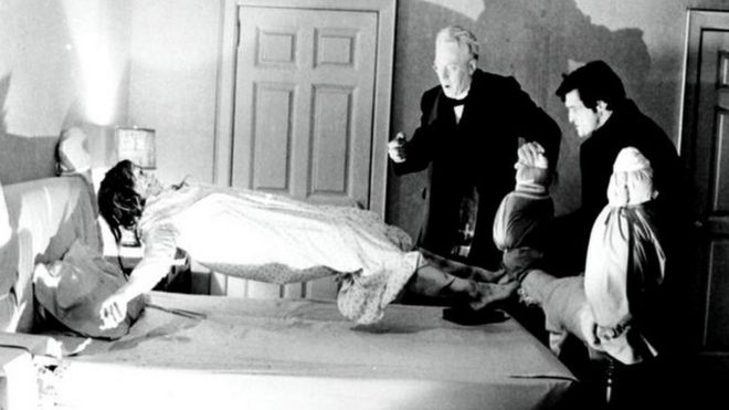 still from The Exorcist in which a girl is levitating as two men watch, looking shocked