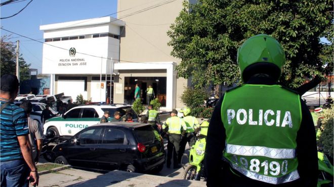 A helmeted policeman in his bright green uniform looks at the police station as medical staff and other officers congregate in front of the station