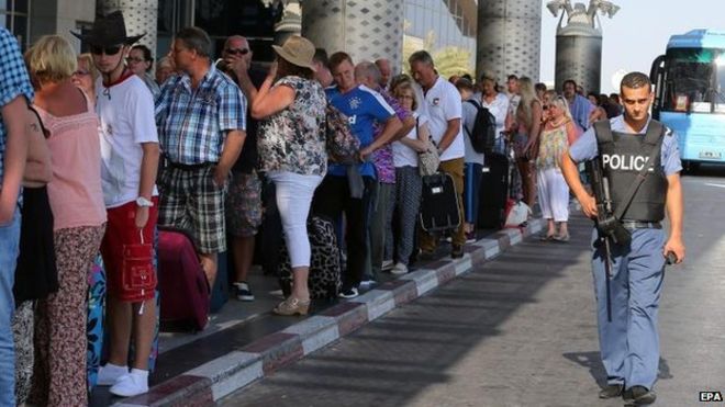 A Tunisian policeman stands guard in front of British tourists at the Enfidha International airport in Sousse, Tunisia