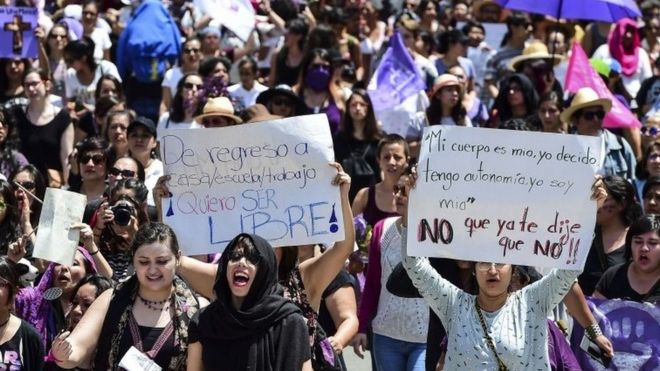 Women carrying banners demanding respect. The signs say "At home, school or work, I want to be free" and "My body is mine. I decide. I said NO"."