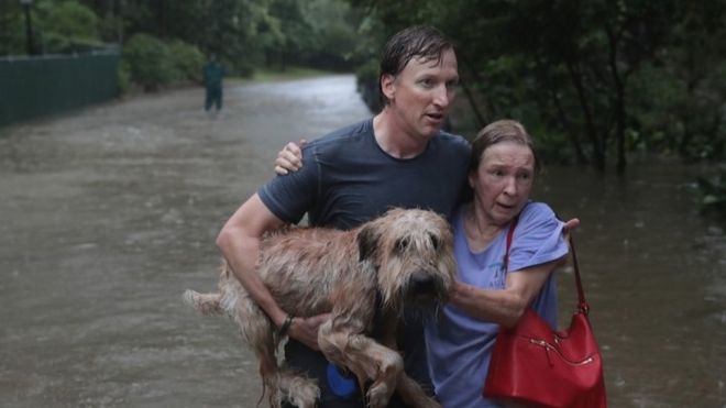 A man helps a neighbour down a street in Houston after rescuing her from her home in his boat in River Oaks, Houston (27 August 2017)