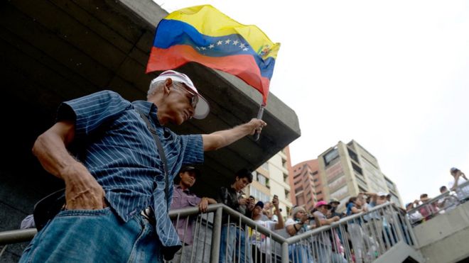 Hombre mayor sostiene bandera de Venezuela.