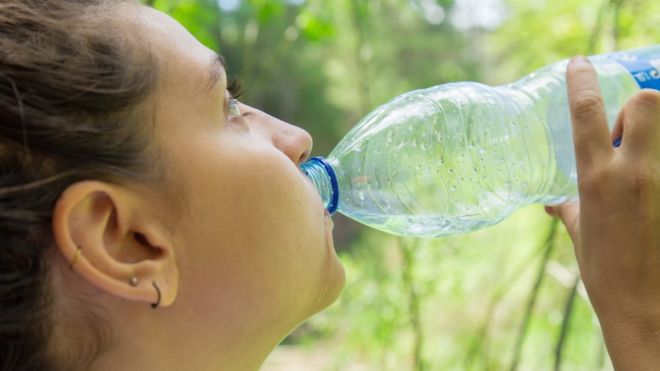 Mujer toma agua en botella de plÃ¡stico.