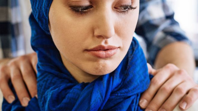 A generic photo a women in a blue headscarf sitting with a man placing his hands on her shoulders