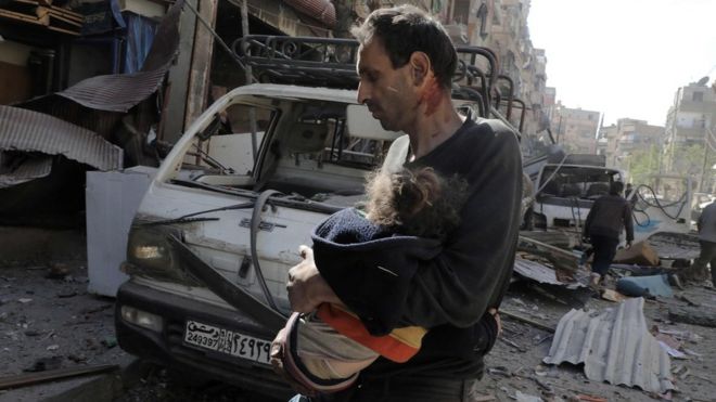A man carries an injured girl following air strikes on the town of Douma, in the rebel-held Eastern Ghouta region (20 March 2018)
