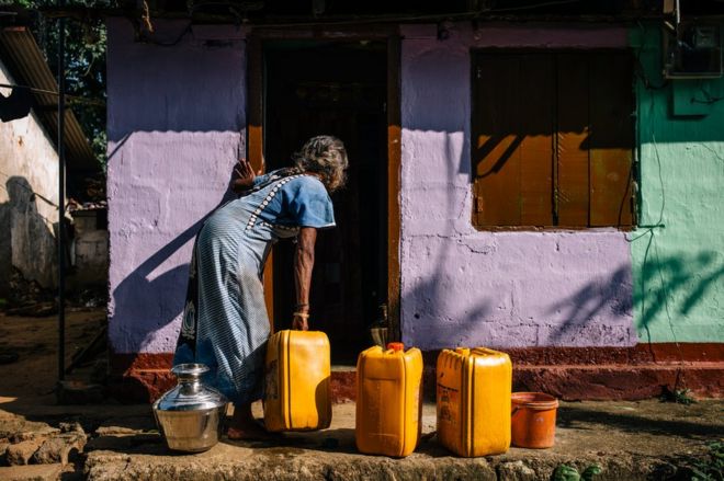 A woman collects water in containers outside her house
